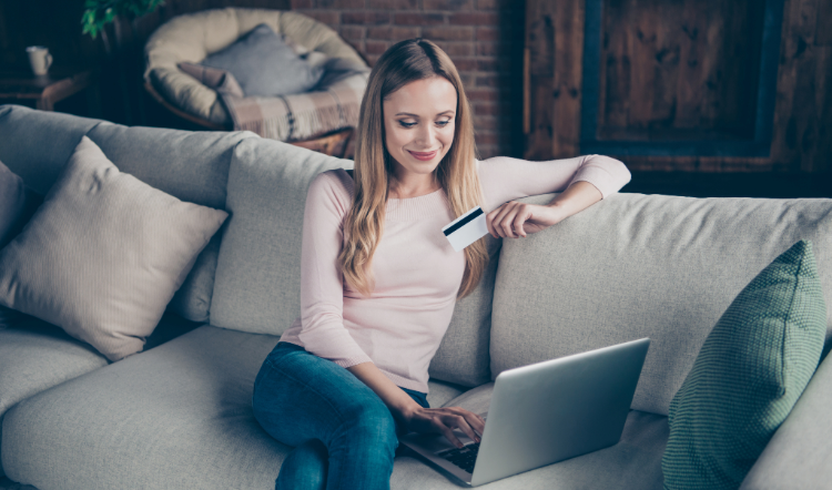 Woman sitting on couch with laptop and debit or credit card in hand.