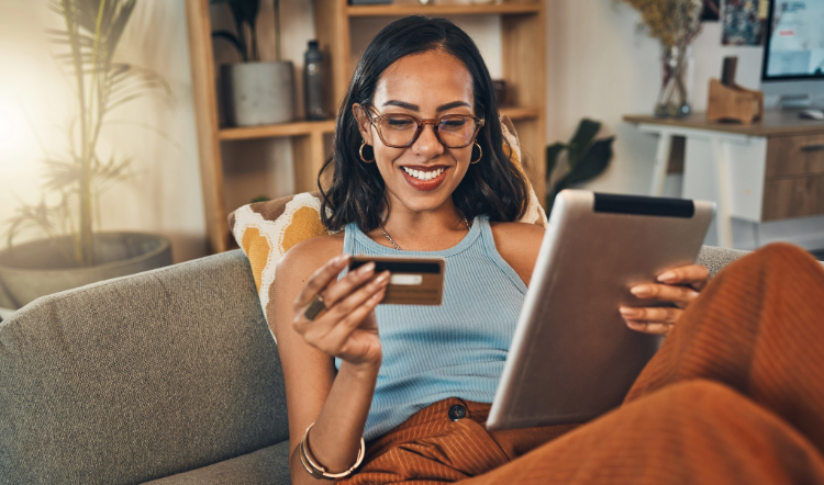 Woman sitting on couch looking at a bank card and tablet in her hands.