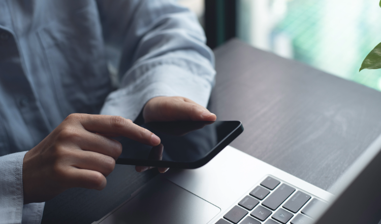 Man is touching his phone screen in front of a laptop.