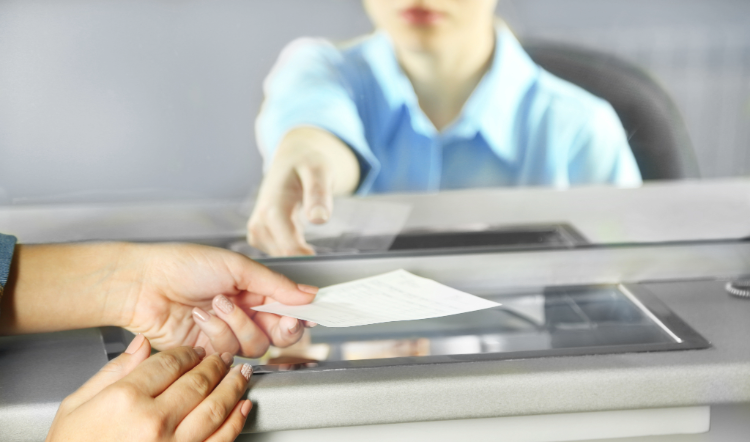 A person slides a check across a counter to a bank teller. 